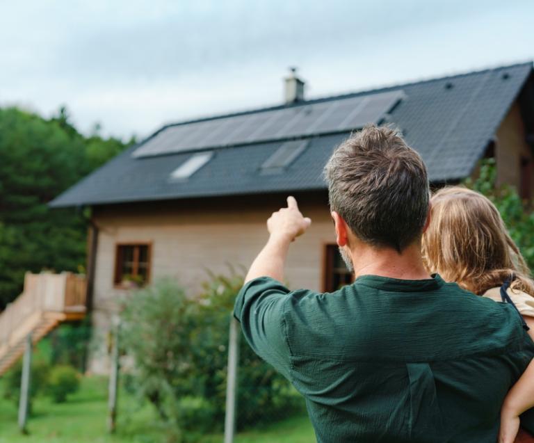 Père et fille devant une maison avec panneaux solaires, symbolisant le projet : investir dans une maison pour une mise en location familiale et durable.