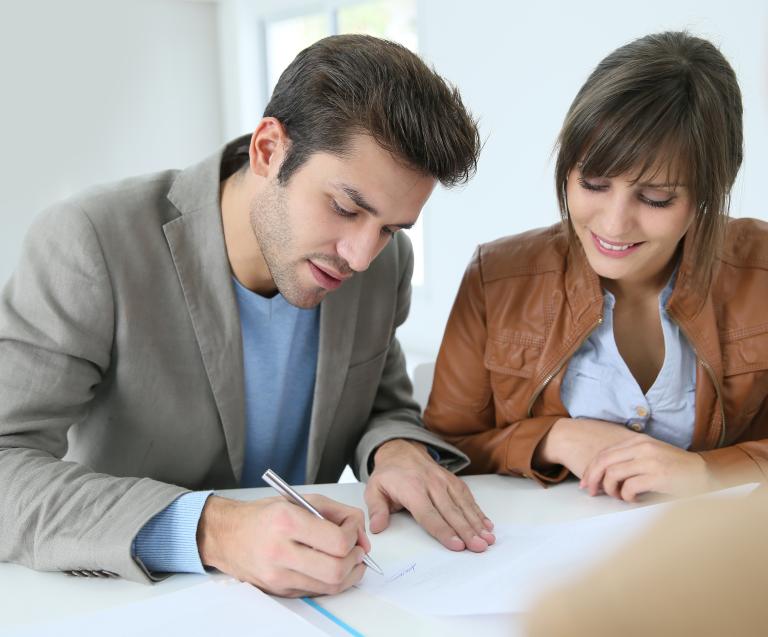 Jeune couple signant un contrat de location avec dépôt de garantie chez un professionnel de la gestion immobilière