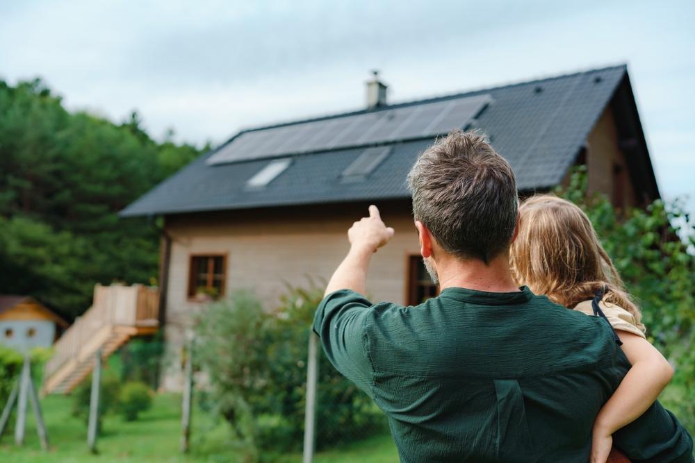 Père et fille devant une maison avec panneaux solaires, symbolisant le projet : investir dans une maison pour une mise en location familiale et durable.