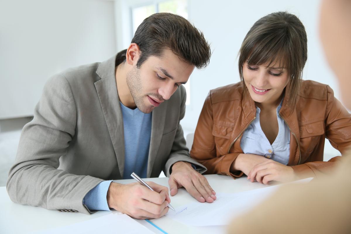 Jeune couple signant un contrat de location avec dépôt de garantie chez un professionnel de la gestion immobilière