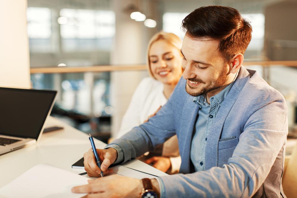 Signature d’un bail d’habitation entre un jeune couple et un professionnel, illustrant les clauses essentielles à insérer dans un contrat de location.
